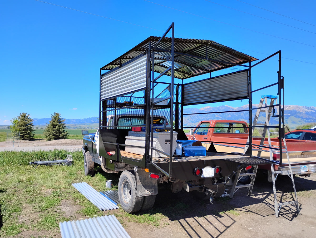 "Custom-built mobile Christian art studio on the back of an old farm truck with metal roof and mesh sides, parked on a Montana farm with mountain views"