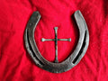 Handmade Christian horseshoe nail cross on red fabric — a single steel horseshoe with a Western cross formed from three horseshoe nails welded in the center, rustic horseshoe halo faith art handmade in Montana