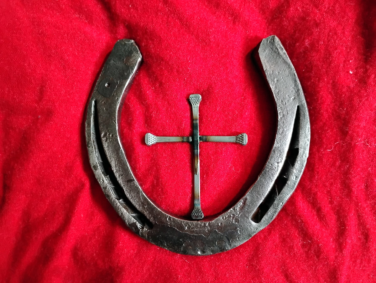 Handmade Christian horseshoe nail cross on red fabric — a single steel horseshoe with a Western cross formed from three horseshoe nails welded in the center, rustic horseshoe halo faith art handmade in Montana