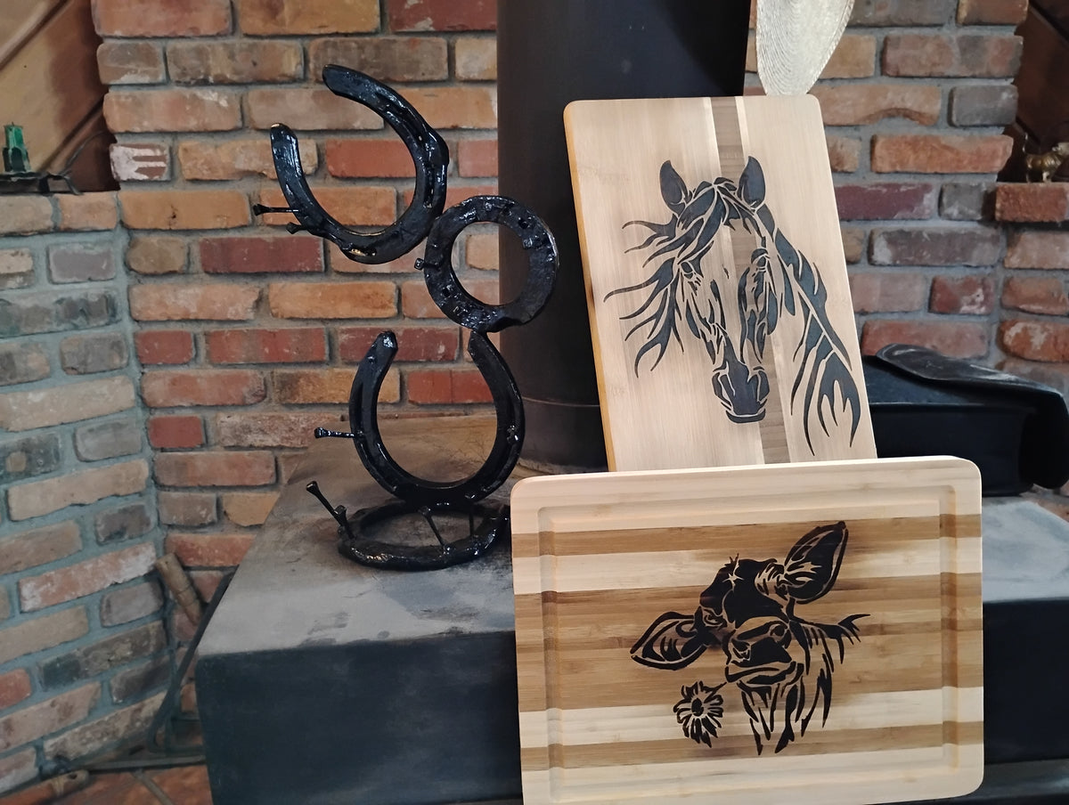 "Handmade horseshoe jewelry holder and picture frame alongside a wood-burned cutting board with horse and cow designs, displayed in a rustic brick fireplace setting"